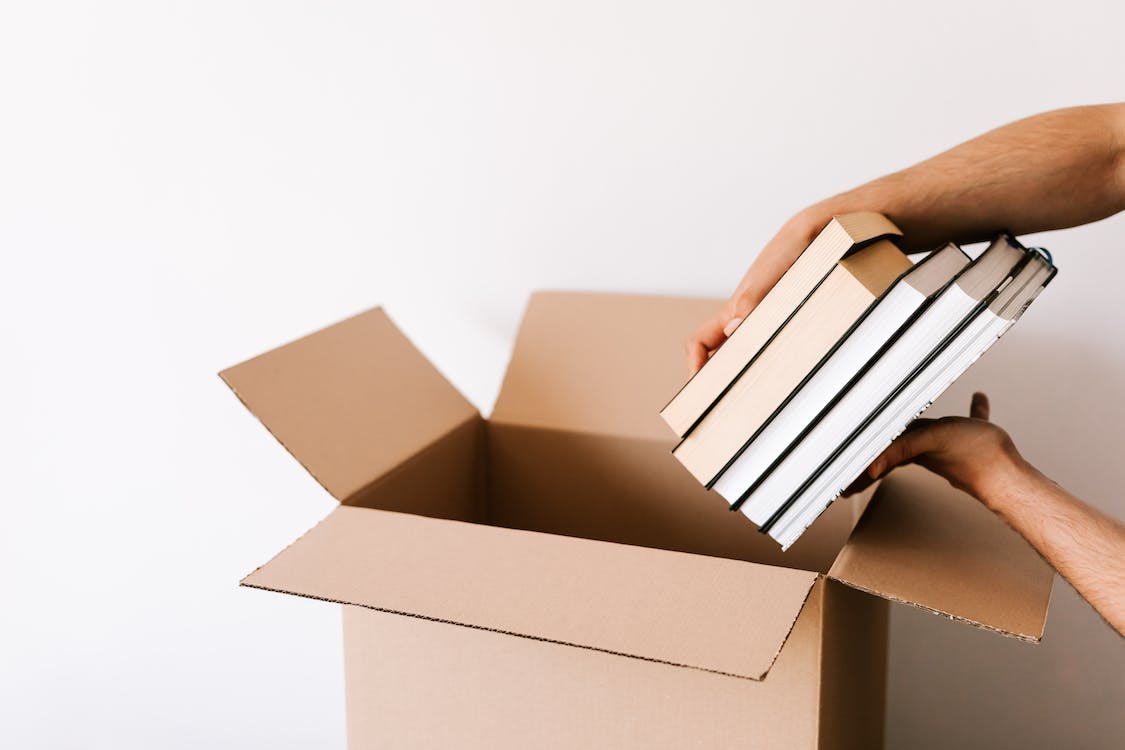 The clean hands of a happy homeowner packs a stack of books into a box